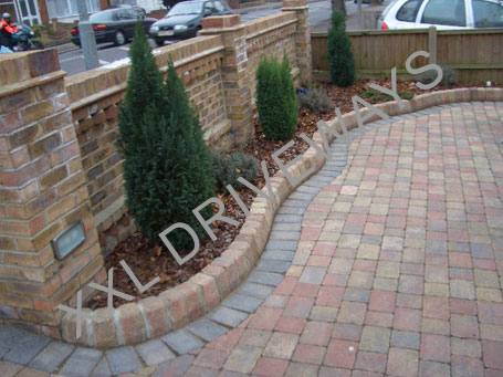 Block paved driveway with flower bed, brick wall surrounding property.